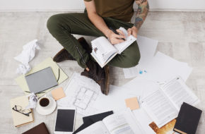 A man writes notes surrounded by devices and paperwork