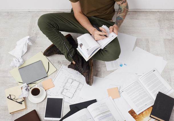 A man writes notes surrounded by devices and paperwork